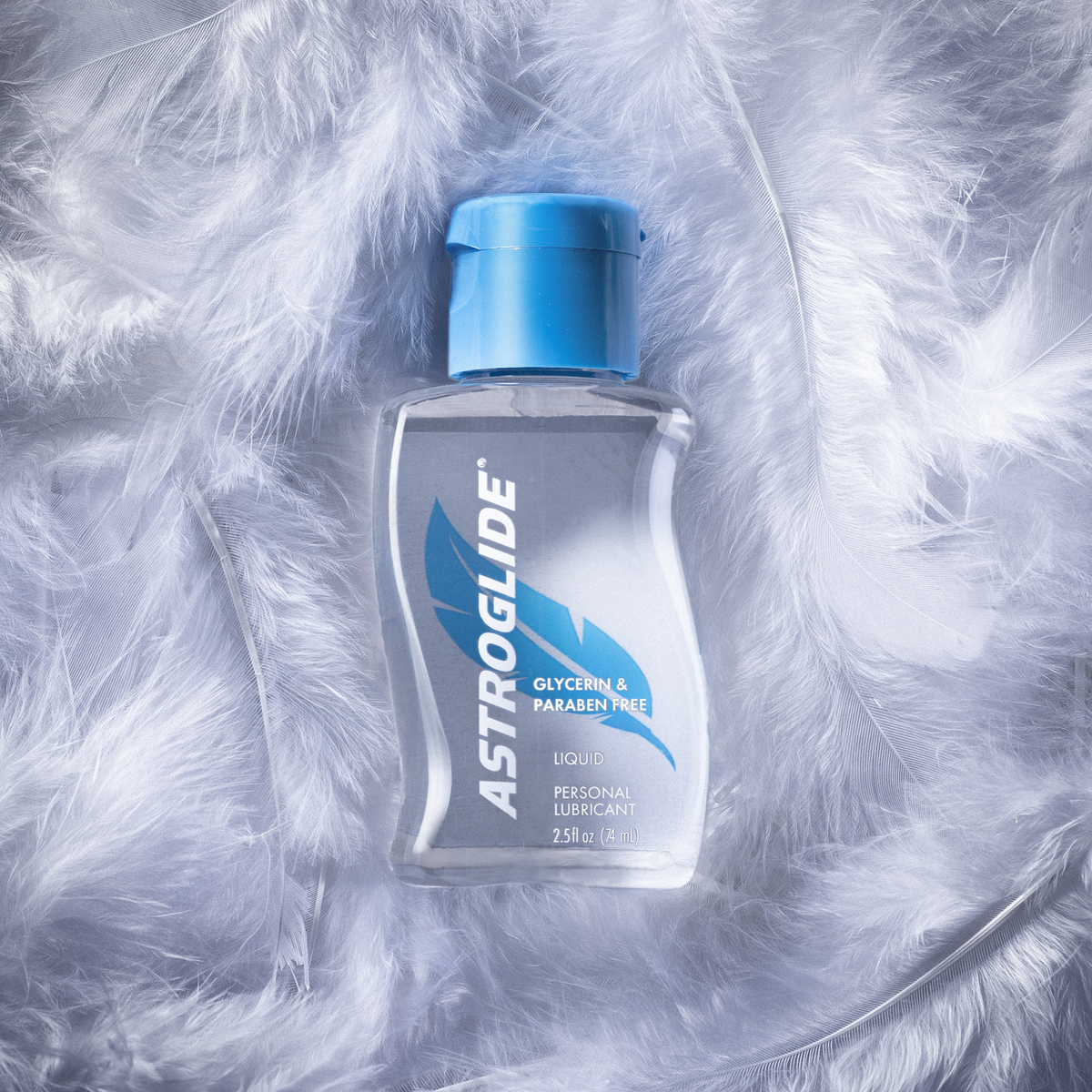 A bottle of Astroglide Glycerin & Paraben Free Liquid Lubricant with a blue cap, resting on a pile of soft white feathers.