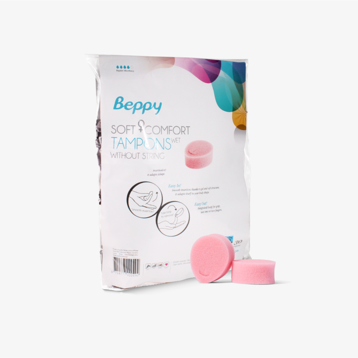 A product shot of the Beppy Soft + Comfort Tampons Wet packaging. The white plastic bag features blue and grey text with colorful abstract shapes at the top. Two loose pink sponges sit in the foreground. Diagrams on the bag illustrate the "Easy In" and "Easy Out" methods using a finger loop.