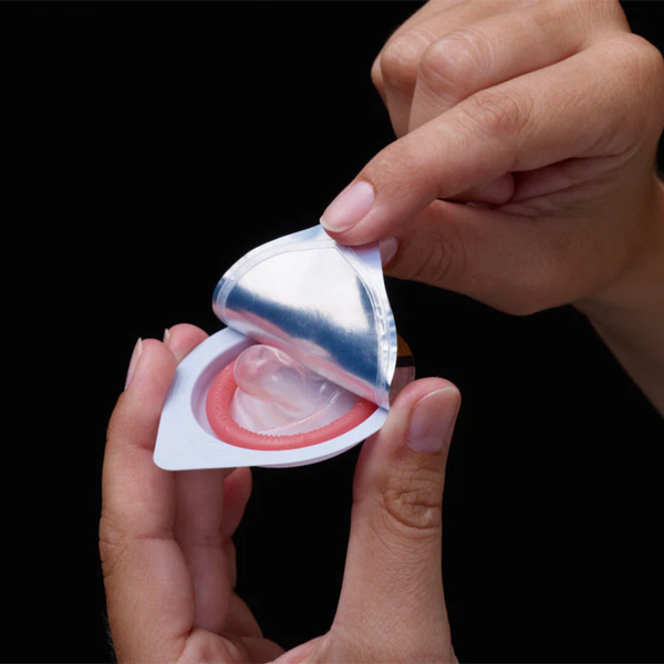 Hands opening a single foil packet to reveal a rolled, lubricated condom. 