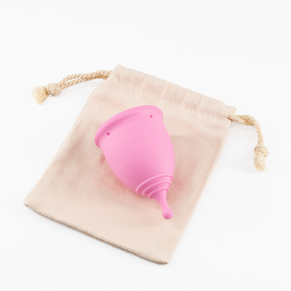 Pink menstrual cup lying next to its light-colored cloth storage bag.