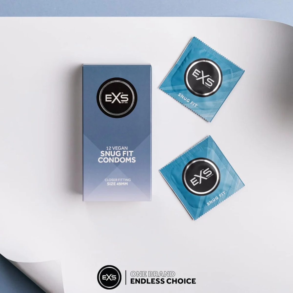 Flat lay photo of the EXS 12 Vegan Snug Fit Condoms box sitting alongside two individual blue foil wrappers on a clean white surface with a soft blue backdrop.