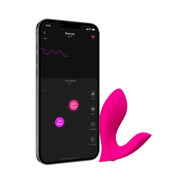 Studio product shot of the bright pink Lovense Flexer dual panty vibrator standing beside a smartphone displaying the Lovense control app interface.