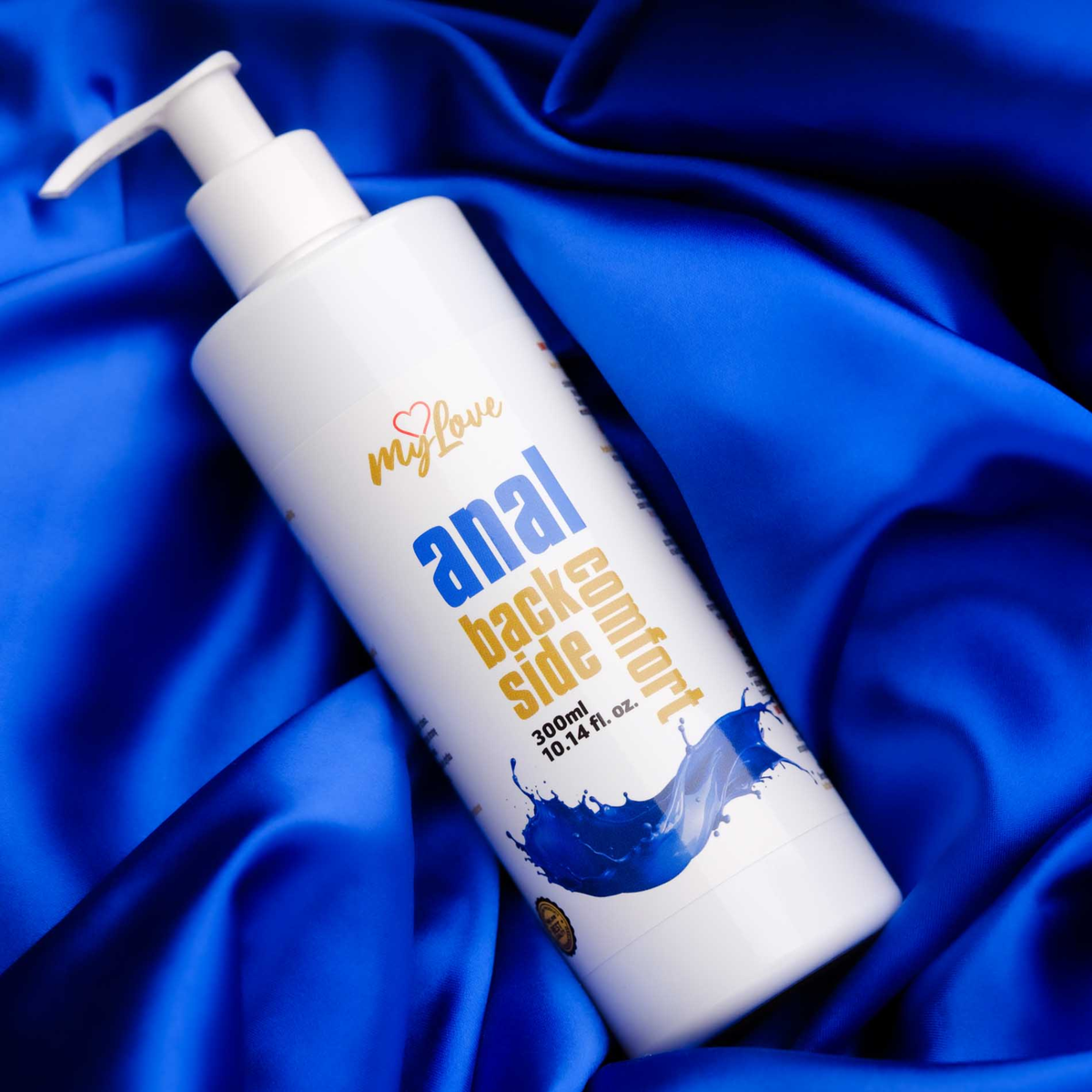 The 300 ml pump bottle of MyLove Anal Back Side Comfort gel rests diagonally on draped, rich royal blue satin fabric.