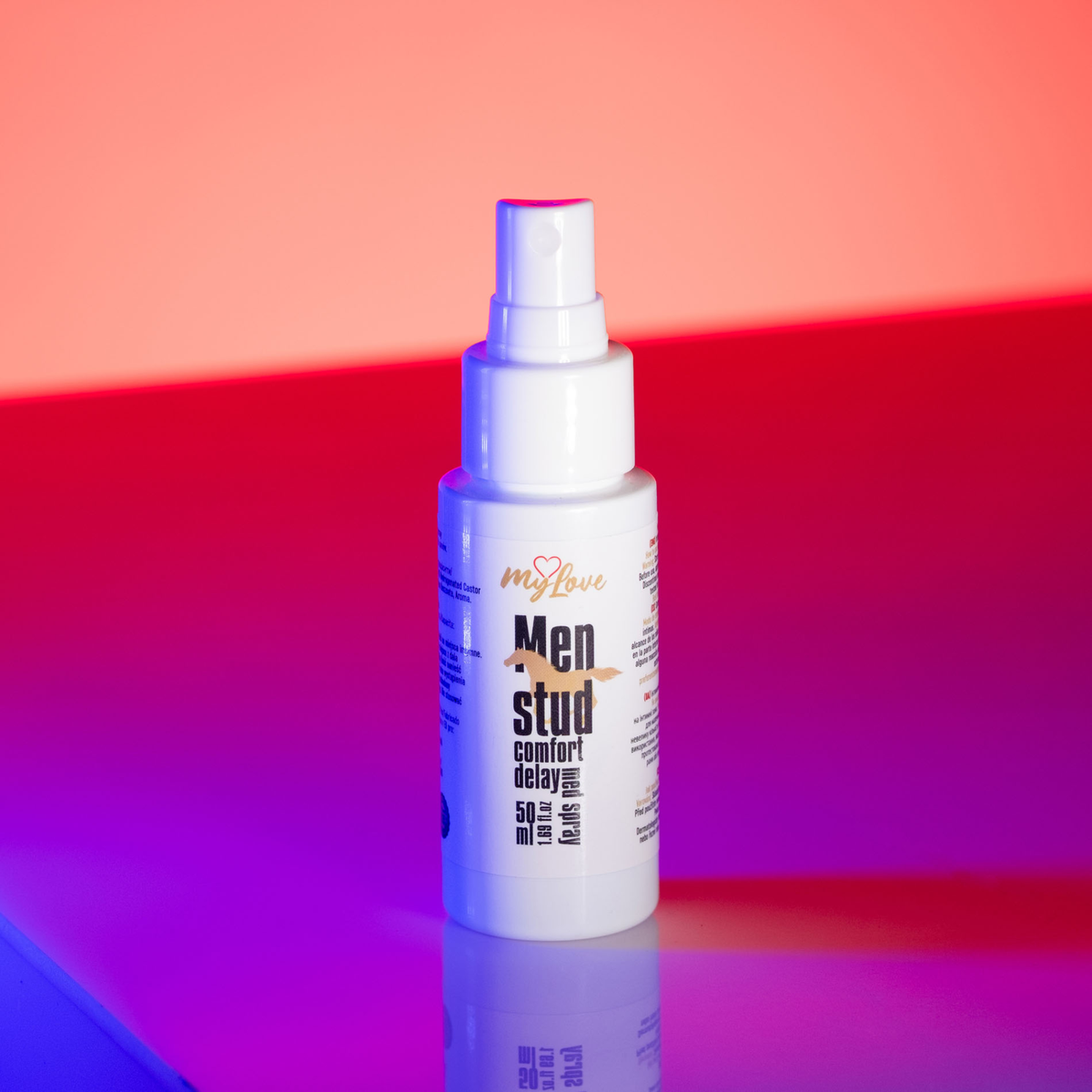 Front view of the 50 ml MyLove Men Stud Comfort Delay Med Spray bottle illuminated under dynamic pink and blue studio lighting.