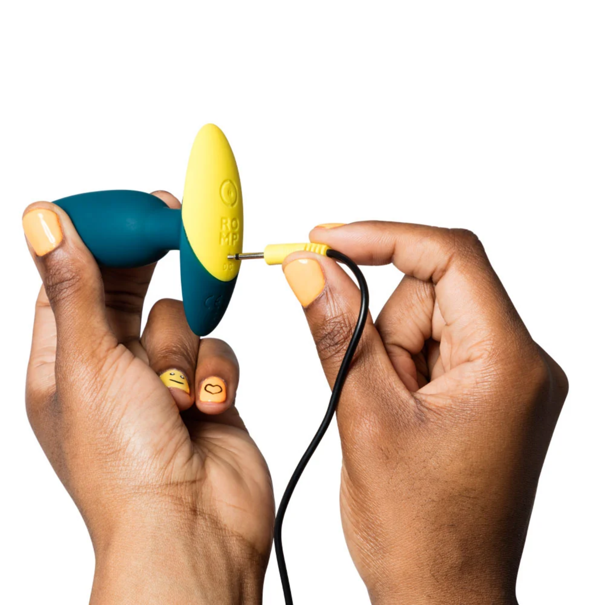 Action photo showing hands plugging the yellow pin charging cable into the DC charging port on the base of the teal ROMP Bass plug.