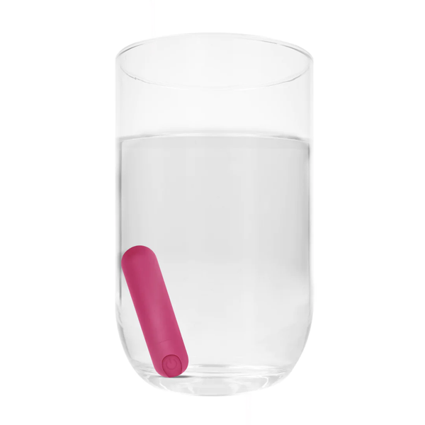 The pink bullet vibrator is shown submerged in a glass of water, illustrating its waterproof feature.