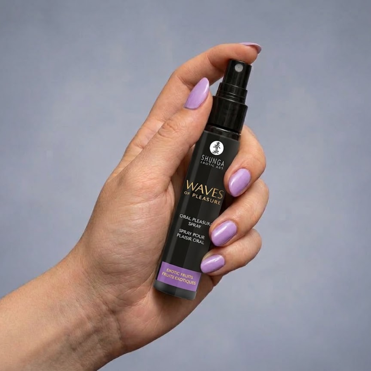 Close-up hand-held shot showing a person with purple-manicured nails holding the black spray bottle against a neutral backdrop.