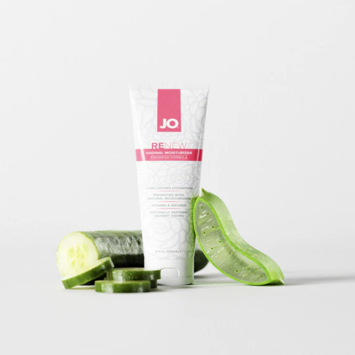 The JO Renew Vaginal Moisturizer tube stands upright on a clean, light grey surface, creatively staged next to fresh cucumber slices and a cut piece of a green aloe vera leaf to highlight its natural ingredients.