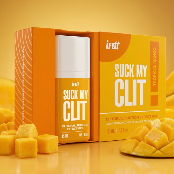 The product bottle, in a bright yellow and white container, is partially pulled out from its open orange and yellow packaging. It is displayed on a glossy yellow surface surrounded by freshly cut, diced mango cubes.