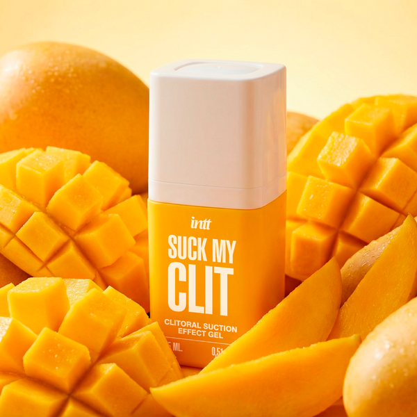 A yellow and white bottle of the intt Suck My Clit clitorial suction gel is nestled closely among a vibrant arrangement of whole, sliced, and cross-hatched cut fresh mangoes.