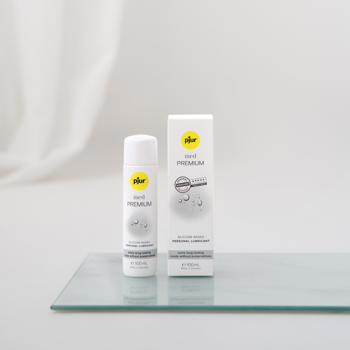 White bottle and box of pjur med PREMIUM silicone-based personal lubricant on a glass surface.