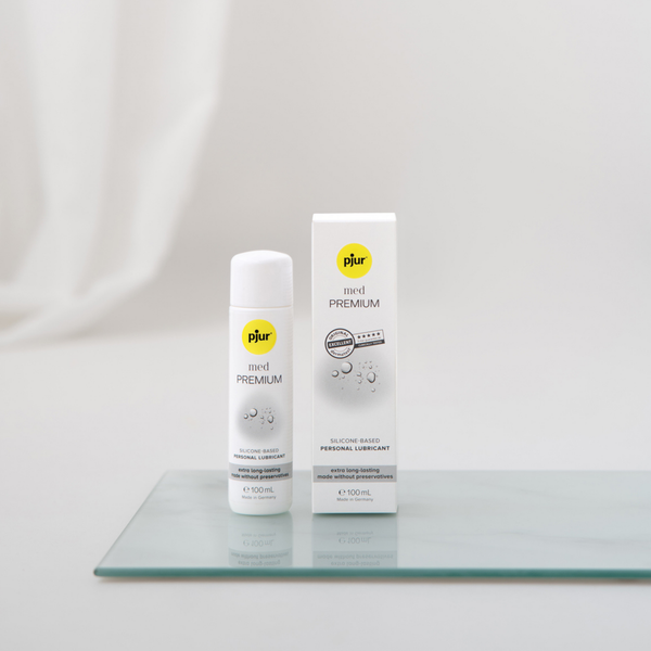 White bottle and box of pjur med PREMIUM silicone-based personal lubricant on a glass surface.