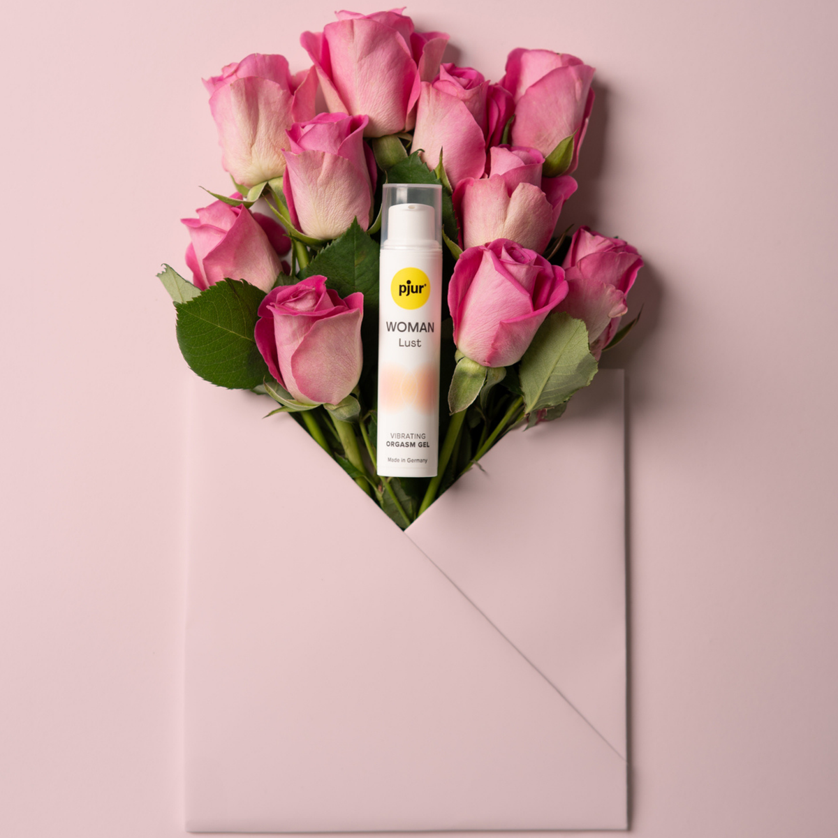 A tube of pjur WOMAN Lust vibrating orgasm gel nestled in a bouquet of pink roses emerging from a light pink envelope.
